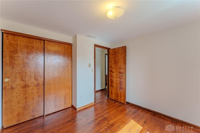 unfurnished bedroom with a closet, visible vents, baseboards, and wood finished floors