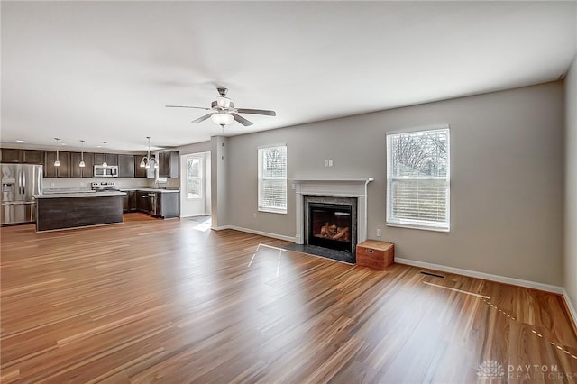 unfurnished living room with wood finished floors, baseboards, a high end fireplace, a sink, and ceiling fan