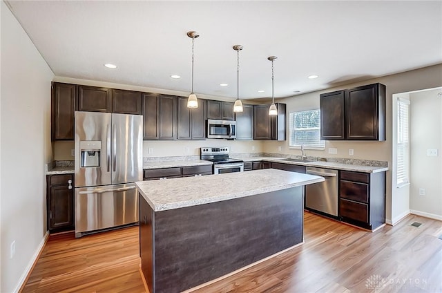 kitchen featuring light wood finished floors, a center island, dark brown cabinetry, appliances with stainless steel finishes, and a sink