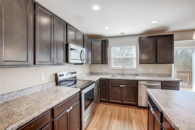 kitchen with a sink, stainless steel appliances, light countertops, dark brown cabinets, and light wood-type flooring