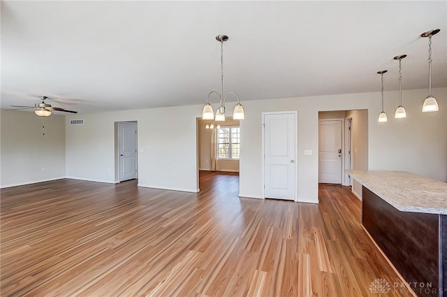 unfurnished living room with visible vents, baseboards, wood finished floors, and ceiling fan with notable chandelier