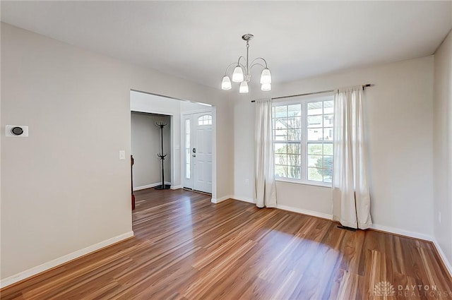 empty room featuring an inviting chandelier, wood finished floors, and baseboards