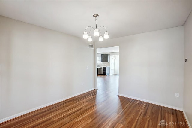 spare room with baseboards, wood finished floors, visible vents, and a chandelier