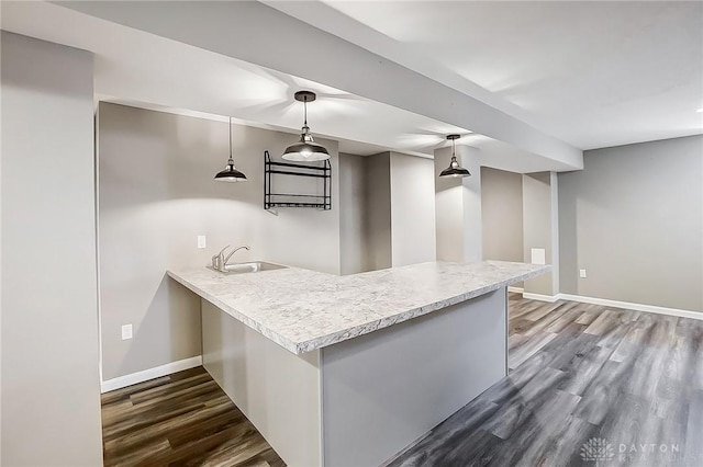 kitchen with baseboards, dark wood finished floors, light countertops, a peninsula, and a sink