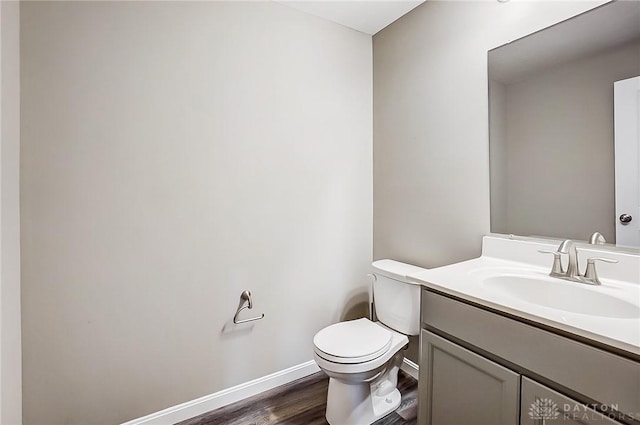 half bathroom with vanity, toilet, wood finished floors, and baseboards