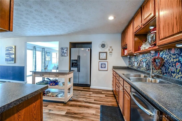 kitchen with dark countertops, dishwasher, stainless steel refrigerator with ice dispenser, dark wood-style floors, and a sink