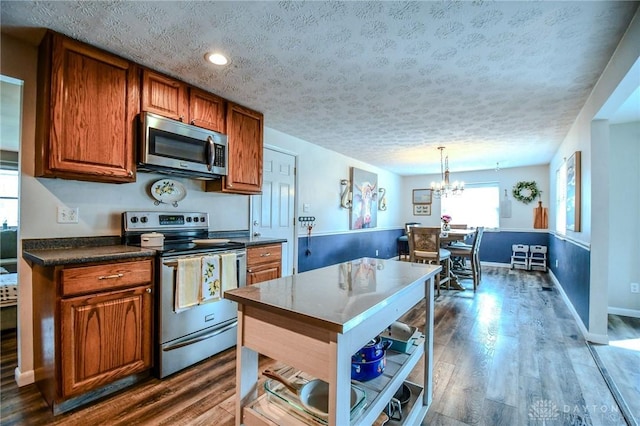 kitchen with brown cabinets, dark countertops, a textured ceiling, stainless steel appliances, and dark wood-style flooring