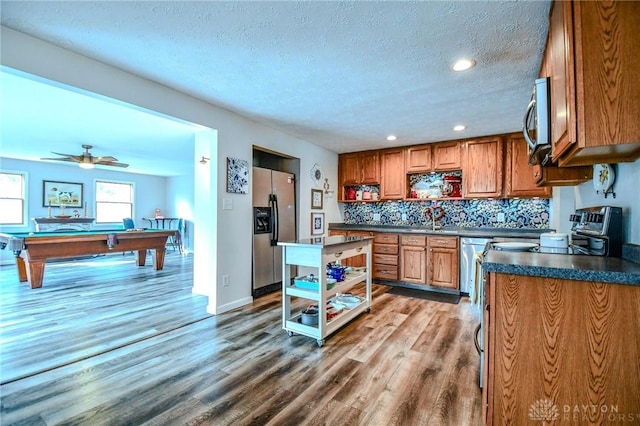 kitchen featuring dark countertops, open shelves, brown cabinetry, stainless steel appliances, and a sink