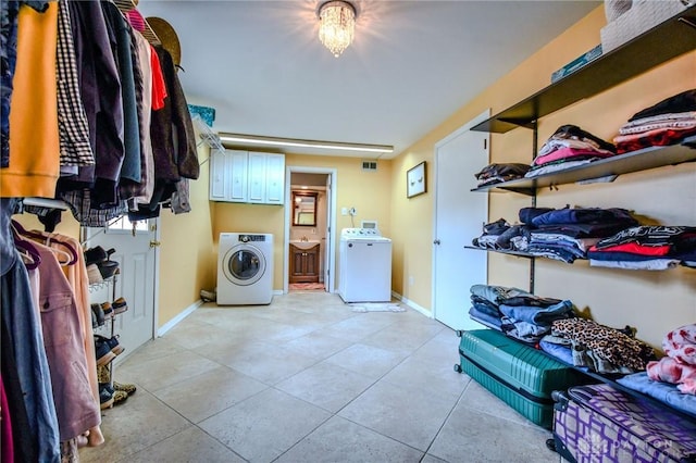 clothes washing area featuring washer / dryer, light tile patterned flooring, cabinet space, and baseboards