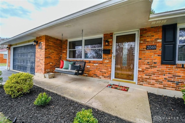 view of exterior entry featuring brick siding, a porch, and a garage