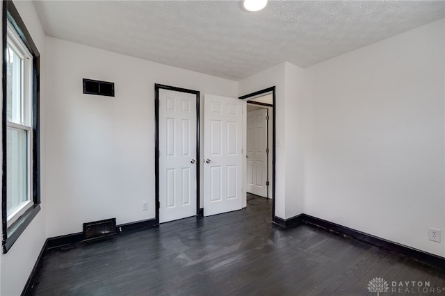 unfurnished bedroom featuring a textured ceiling, dark wood-type flooring, and baseboards