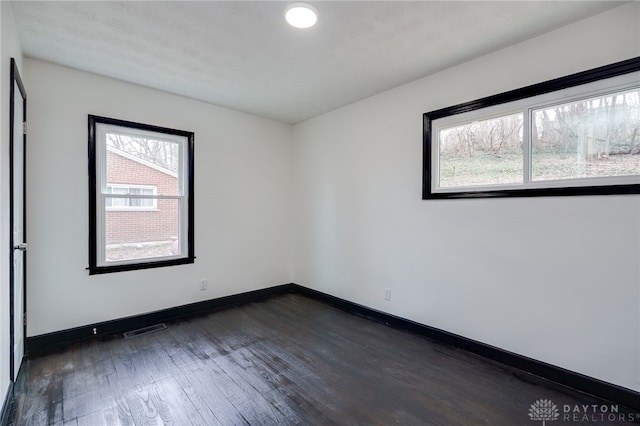 unfurnished room with visible vents, baseboards, and dark wood-style floors