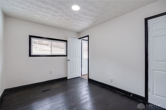 spare room with dark wood-style floors, baseboards, visible vents, and a textured ceiling