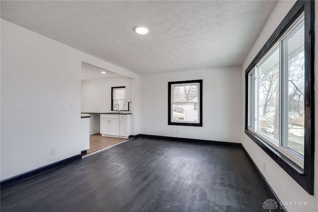 spare room with plenty of natural light, baseboards, dark wood-style flooring, and a textured ceiling