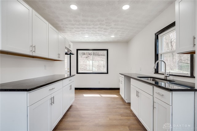 kitchen with dark countertops, light wood finished floors, a textured ceiling, and a sink