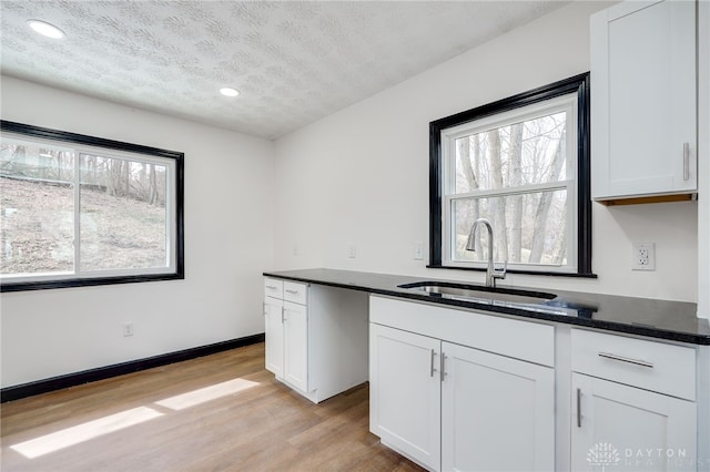 kitchen featuring baseboards, light wood finished floors, a sink, a textured ceiling, and white cabinetry