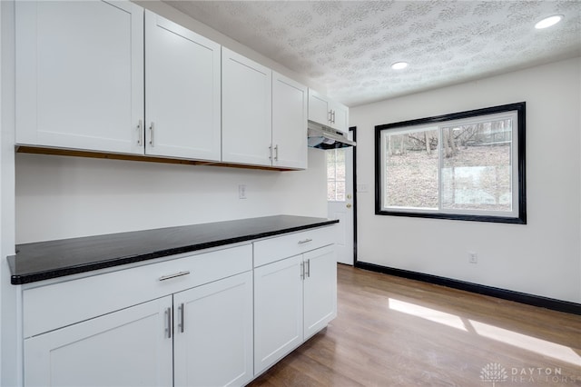 kitchen featuring dark countertops, white cabinets, a textured ceiling, and wood finished floors