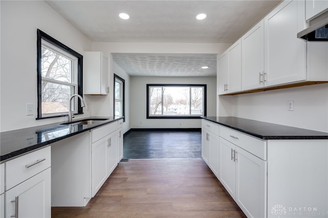 kitchen featuring wall chimney exhaust hood, white cabinetry, dark wood-type flooring, and a sink