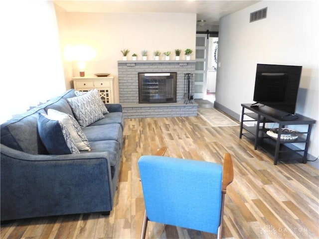 living area featuring wood finished floors, visible vents, baseboards, a fireplace, and a barn door