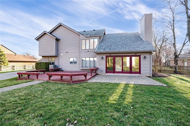 back of property with fence, a shingled roof, a chimney, a deck, and a lawn