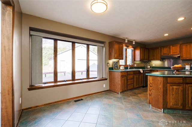 kitchen featuring dark countertops, baseboards, brown cabinets, and under cabinet range hood