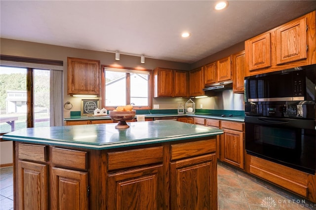 kitchen with black appliances, plenty of natural light, under cabinet range hood, and a kitchen island