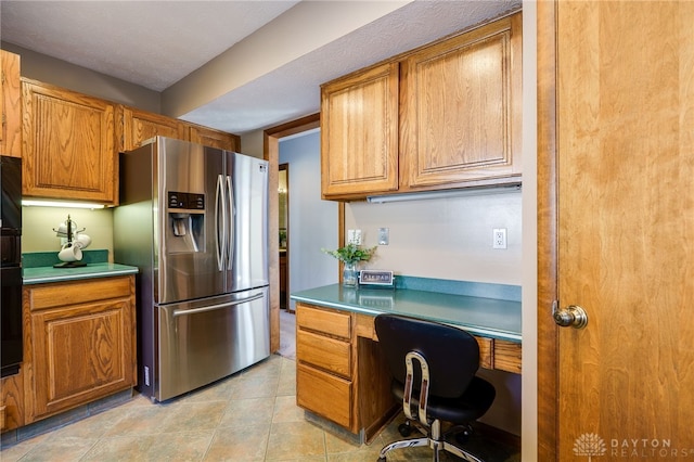 kitchen featuring light tile patterned floors, built in study area, light countertops, stainless steel refrigerator with ice dispenser, and brown cabinets