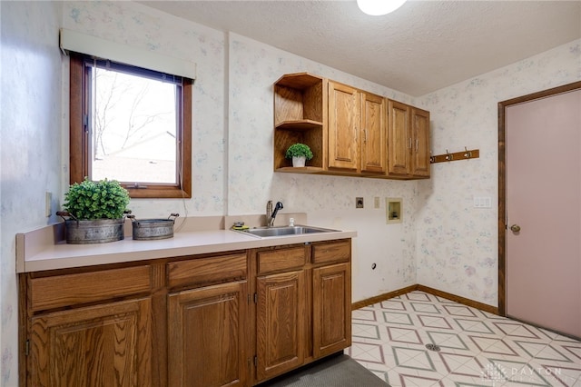 kitchen featuring a textured ceiling, wallpapered walls, and a sink