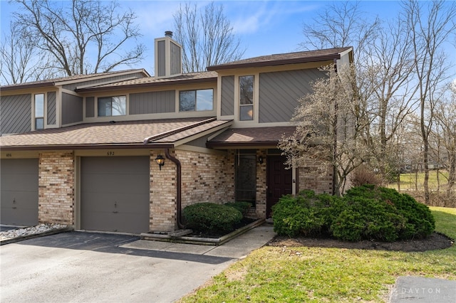 view of property featuring brick siding, driveway, a garage, and roof with shingles