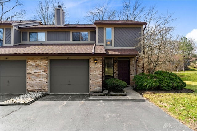 multi unit property featuring aphalt driveway, an attached garage, brick siding, and a chimney