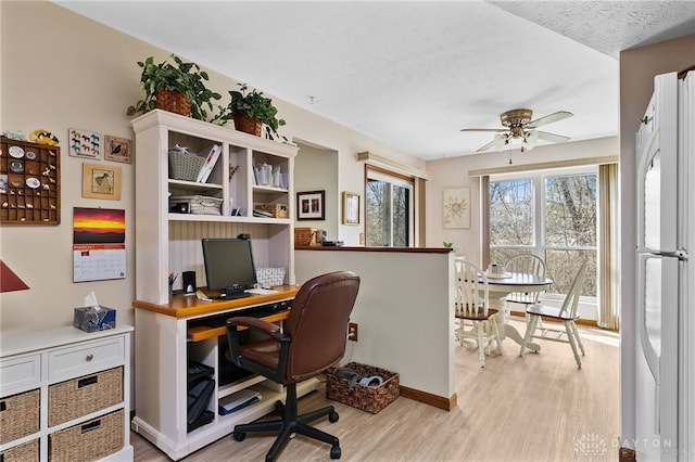 home office featuring light wood finished floors, baseboards, a textured ceiling, and ceiling fan