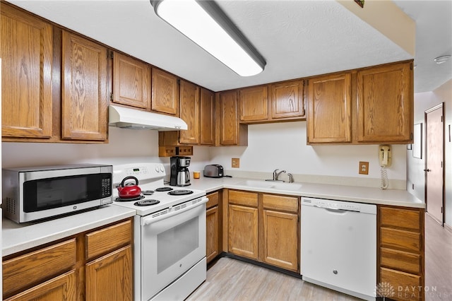 kitchen featuring under cabinet range hood, light countertops, brown cabinetry, white appliances, and a sink