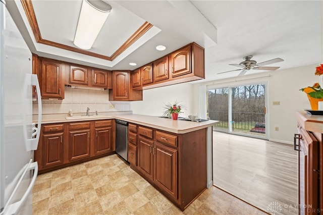 kitchen featuring a peninsula, freestanding refrigerator, a raised ceiling, a ceiling fan, and stainless steel dishwasher