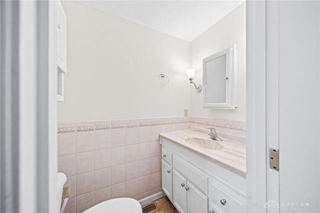 half bath featuring visible vents, a wainscoted wall, toilet, vanity, and tile walls