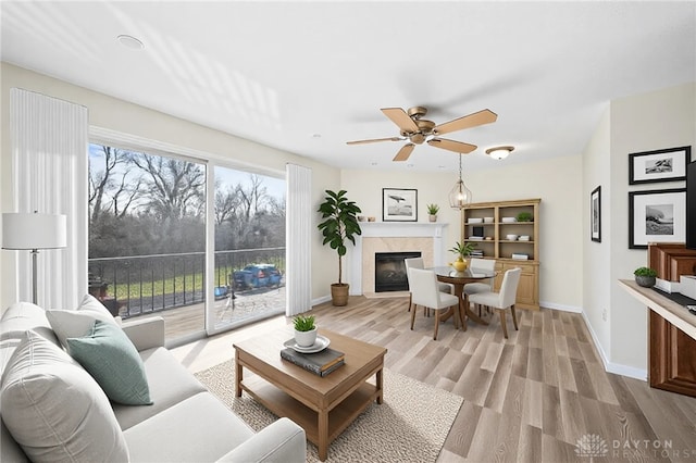 living area featuring a glass covered fireplace, light wood-style flooring, a ceiling fan, and baseboards