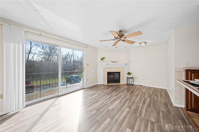 unfurnished living room featuring a tiled fireplace, baseboards, ceiling fan, and wood finished floors