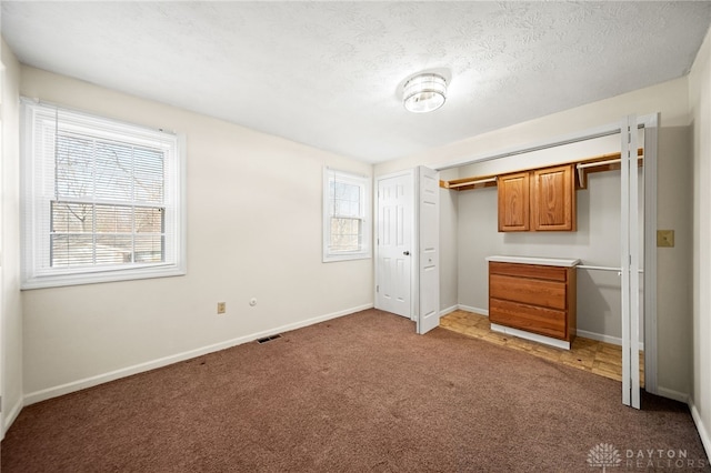 unfurnished bedroom featuring baseboards, visible vents, a closet, a textured ceiling, and carpet flooring