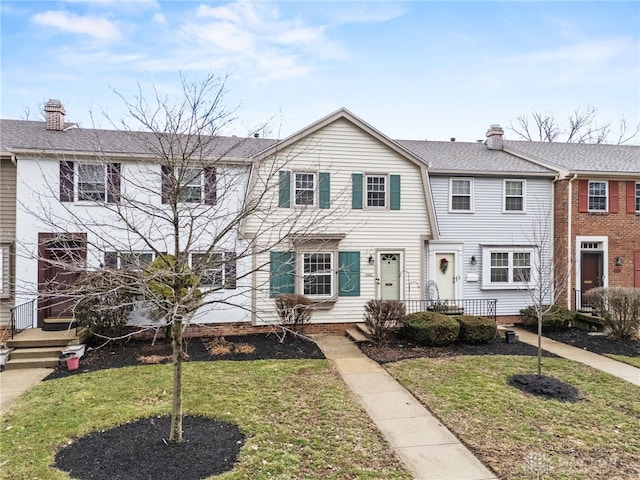 townhome / multi-family property with a chimney, a front lawn, and a shingled roof