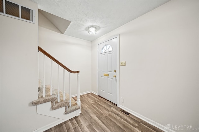 entryway featuring visible vents, a textured ceiling, stairs, and wood finished floors