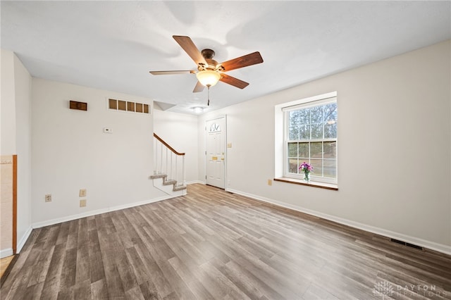 unfurnished living room with ceiling fan, visible vents, wood finished floors, and stairs