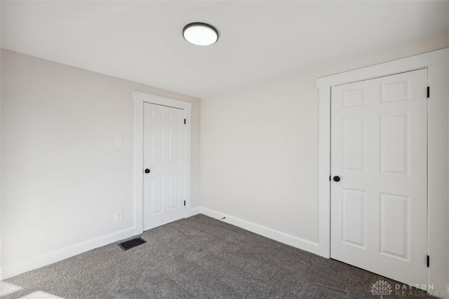 empty room featuring visible vents, baseboards, and dark carpet