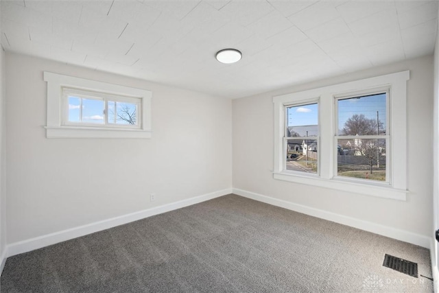 unfurnished room featuring visible vents, dark carpet, and baseboards