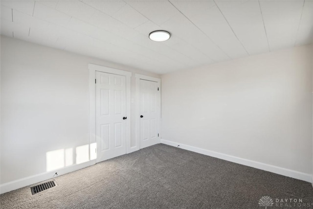 empty room with baseboards, visible vents, and dark carpet