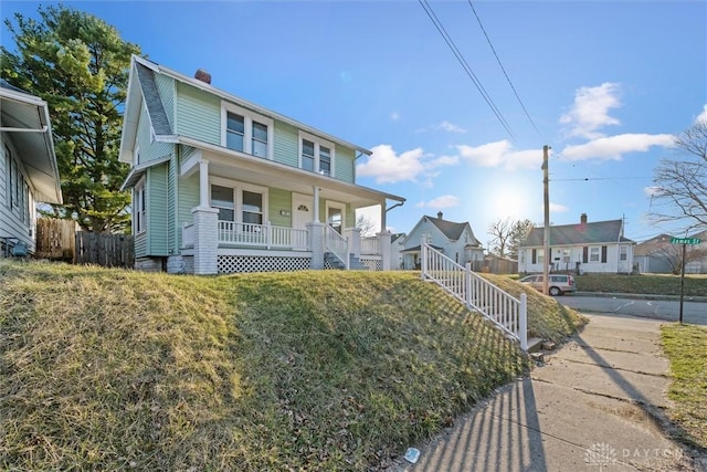 view of front of house featuring a porch, stairway, fence, and a chimney