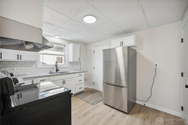 kitchen featuring decorative backsplash, white cabinetry, freestanding refrigerator, and a sink