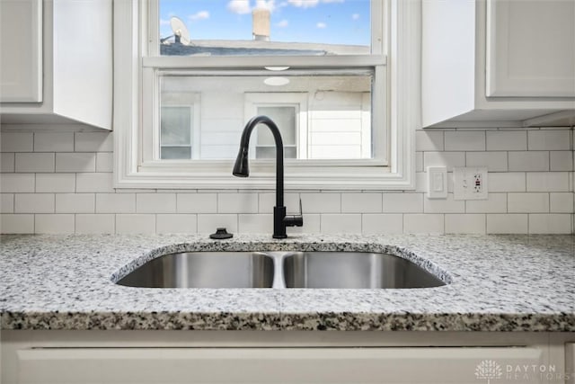 room details featuring light stone counters, backsplash, white cabinets, and a sink