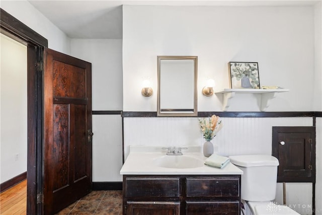 bathroom featuring vanity, toilet, and a wainscoted wall