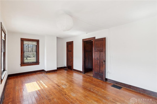 spare room with hardwood / wood-style floors, baseboards, and visible vents