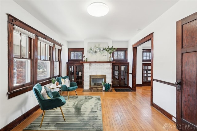 living area with a brick fireplace, baseboards, and light wood-type flooring