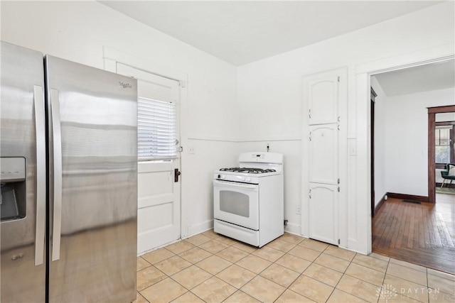 kitchen with light tile patterned floors, baseboards, stainless steel fridge, and white range with gas stovetop